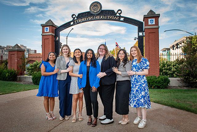 Seven professionally-dressed young women standing in front of the 博彩网址大全 archway